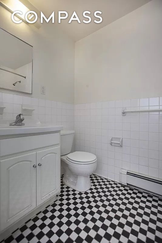 bathroom with tile walls, a baseboard radiator, toilet, wainscoting, and vanity