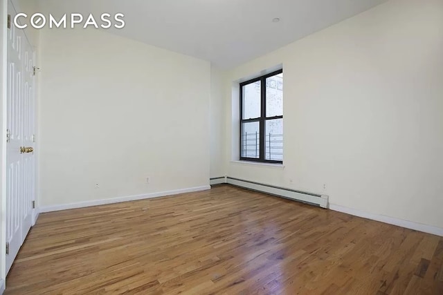 spare room with baseboard heating, wood finished floors, and baseboards