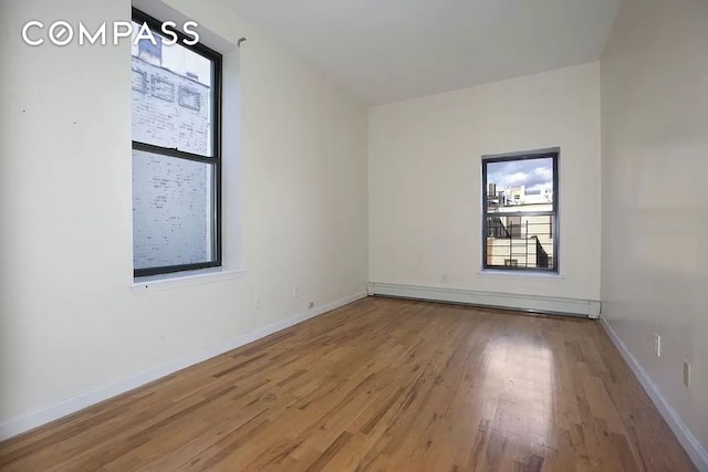 spare room featuring light wood-type flooring, a baseboard radiator, and baseboards