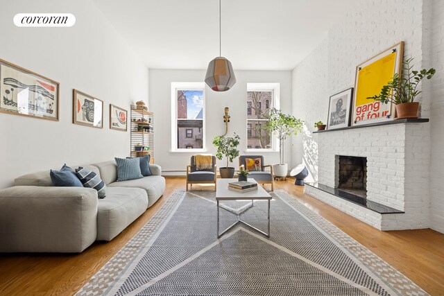 living area with a brick fireplace, visible vents, wood finished floors, and a baseboard heating unit