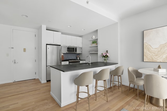 kitchen featuring a breakfast bar area, dark countertops, light wood-style flooring, appliances with stainless steel finishes, and a sink