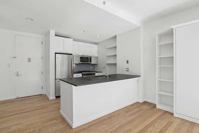 kitchen with white cabinets, appliances with stainless steel finishes, a peninsula, open shelves, and a sink