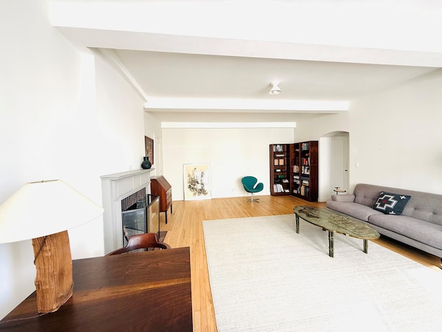 living room with arched walkways, beam ceiling, a fireplace, and wood finished floors