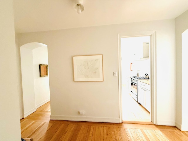 hall with arched walkways, baseboards, and light wood-style floors