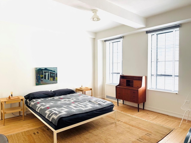 bedroom with beam ceiling, baseboards, and wood finished floors