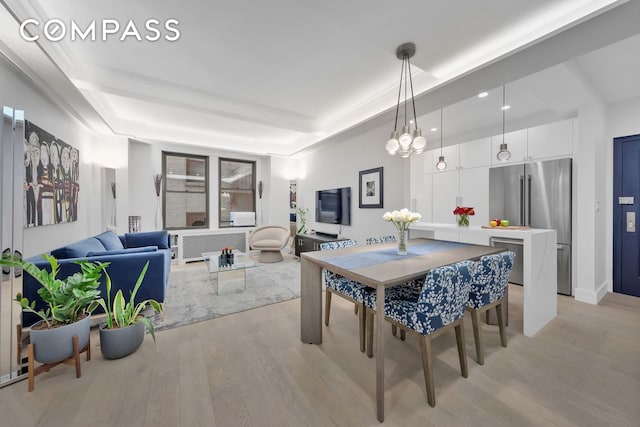 dining area with light wood-style flooring, a raised ceiling, and radiator heating unit