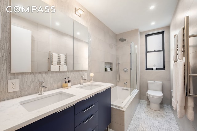 full bathroom with tile walls, toilet, washtub / shower combination, double vanity, and tile patterned floors