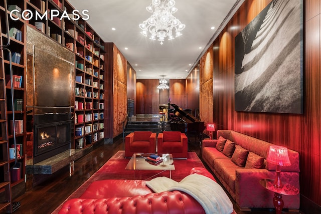interior space with a chandelier, built in features, wood-type flooring, a lit fireplace, and wooden walls