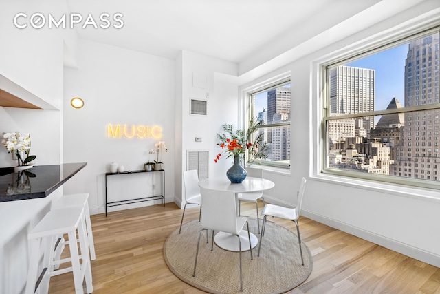 dining room with light wood-style flooring, visible vents, a city view, and baseboards