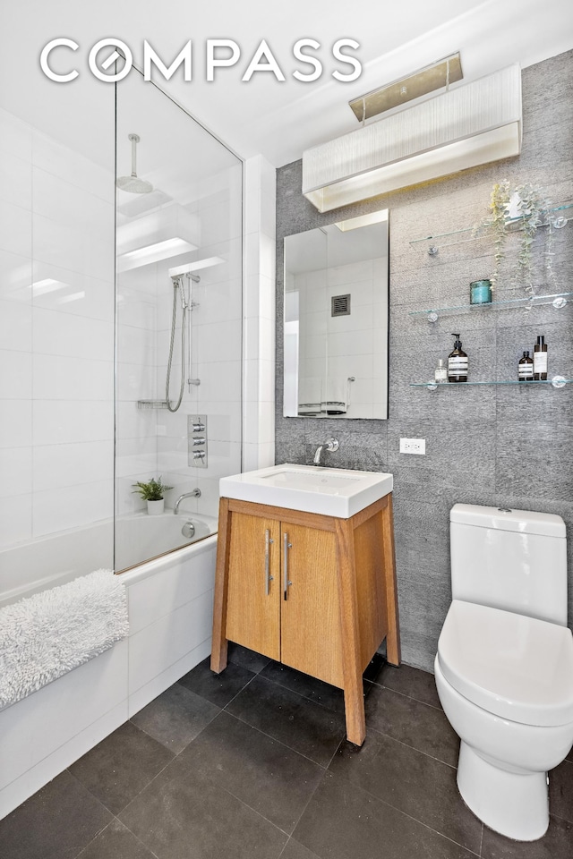 bathroom featuring a combined bath / shower with rainfall shower, toilet, tile walls, vanity, and tile patterned flooring