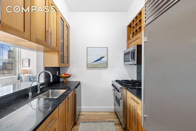 kitchen with dark stone countertops, light wood-style floors, high quality appliances, a sink, and baseboards
