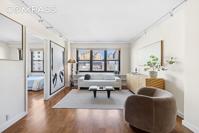 living area with rail lighting, wood finished floors, and baseboards