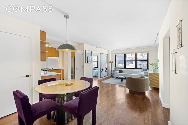 dining space featuring rail lighting, wood finished floors, and baseboards