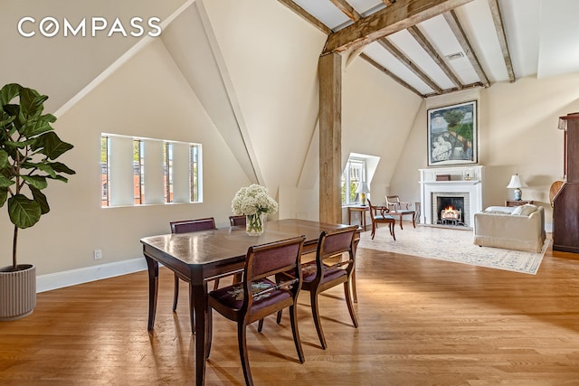 dining room with a brick fireplace, wood finished floors, high vaulted ceiling, beamed ceiling, and baseboards