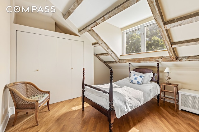 bedroom with vaulted ceiling with beams, a closet, wood finished floors, and radiator