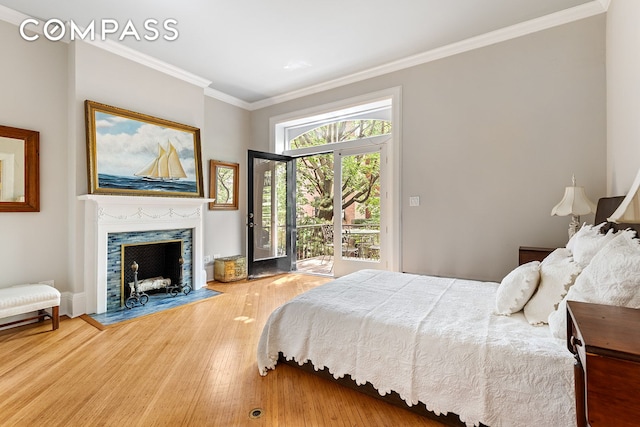 bedroom with access to outside, a fireplace, wood finished floors, and crown molding