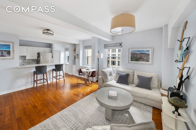 living area featuring beam ceiling, baseboards, and hardwood / wood-style flooring