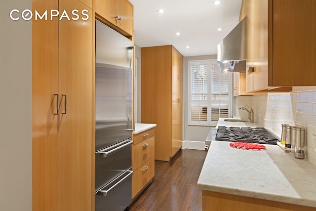 kitchen featuring decorative backsplash, dark wood-type flooring, extractor fan, a sink, and built in fridge