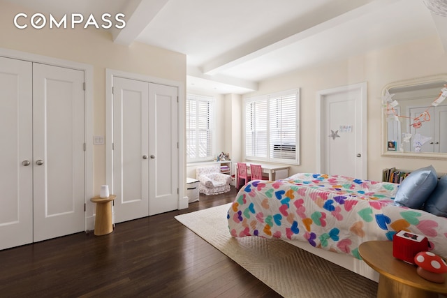 bedroom with two closets, dark wood-style flooring, and beamed ceiling