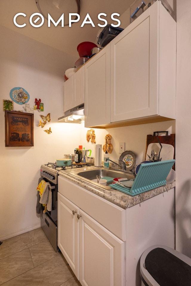 kitchen featuring light countertops, under cabinet range hood, stainless steel range with gas cooktop, white cabinetry, and a sink