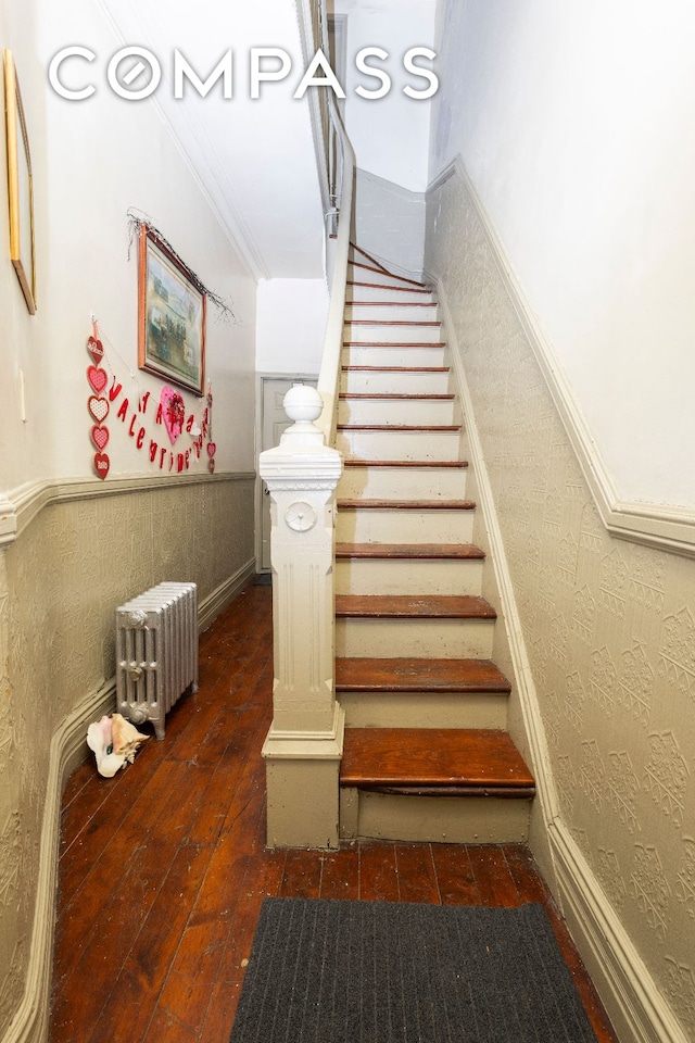 stairs with ornamental molding, a wainscoted wall, radiator heating unit, and hardwood / wood-style flooring