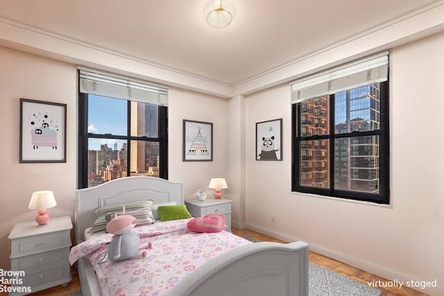 bedroom with a view of city, wood finished floors, and baseboards