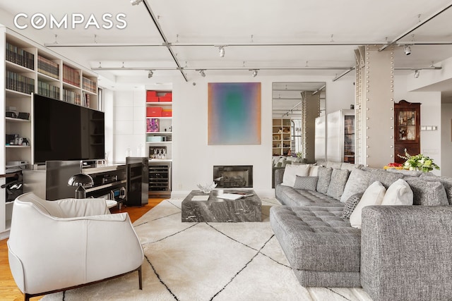 living room with a glass covered fireplace, wine cooler, wood finished floors, and rail lighting