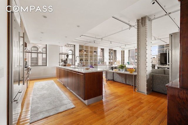 kitchen with a center island with sink, light countertops, light wood-style flooring, open floor plan, and a sink