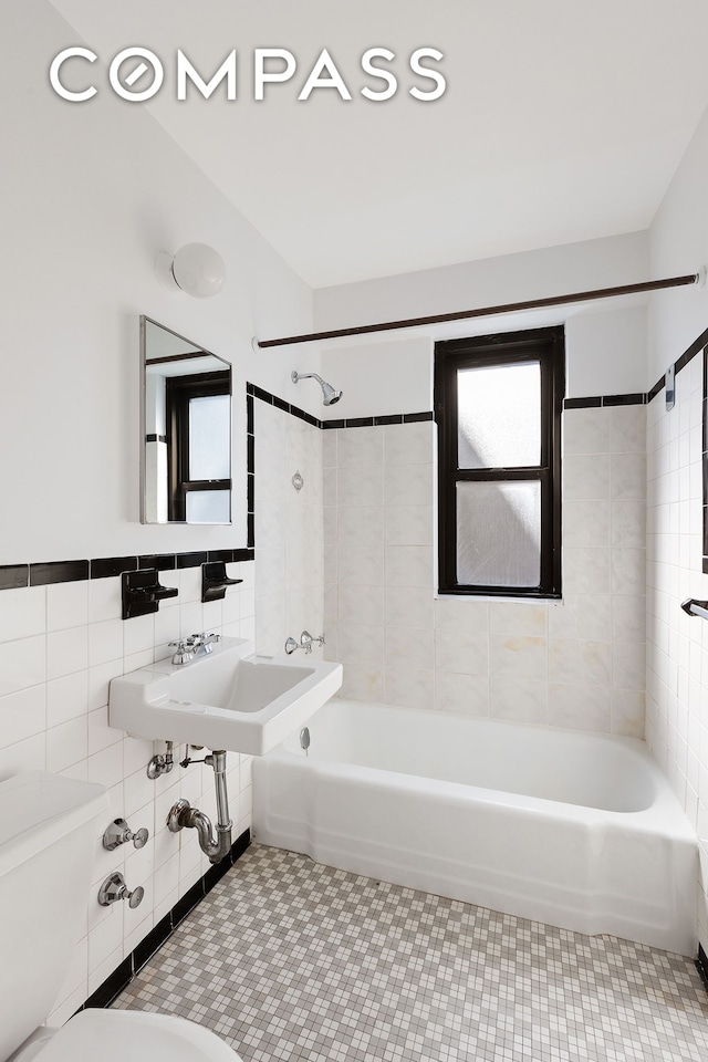 bathroom with tile walls, a sink, tile patterned floors, toilet, and tub / shower combination