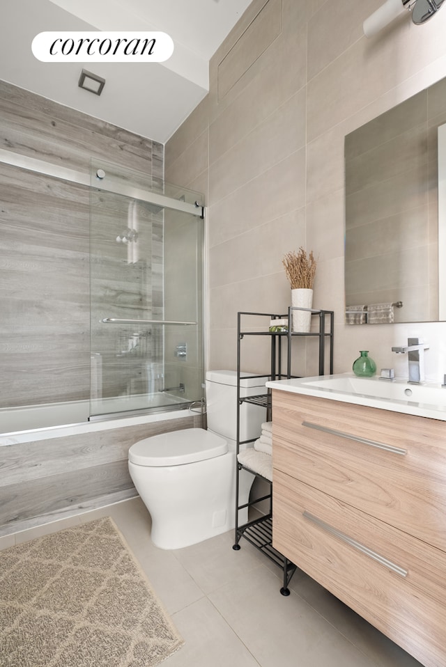 full bathroom featuring toilet, shower / bath combination with glass door, tile patterned floors, vanity, and tile walls