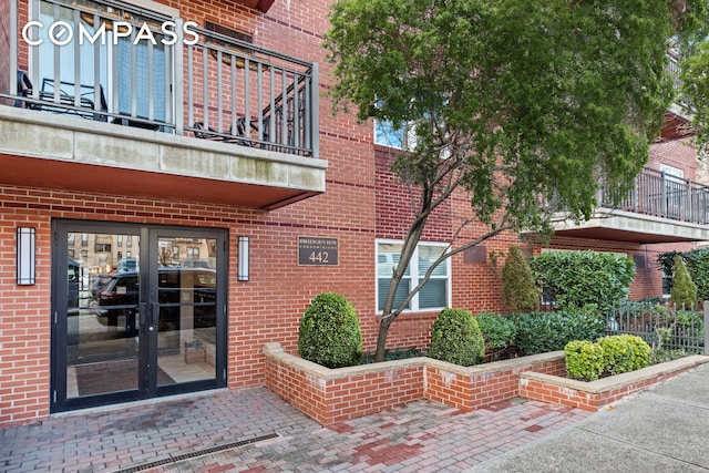 exterior space with a balcony, french doors, and brick siding