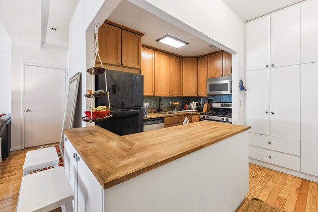69 E 130th St Unit 1C, New York City, NY 10037 - kitchen featuring decorative backsplash, light wood-type flooring, brown cabinets, wood counters, and appliances with stainless steel finishes