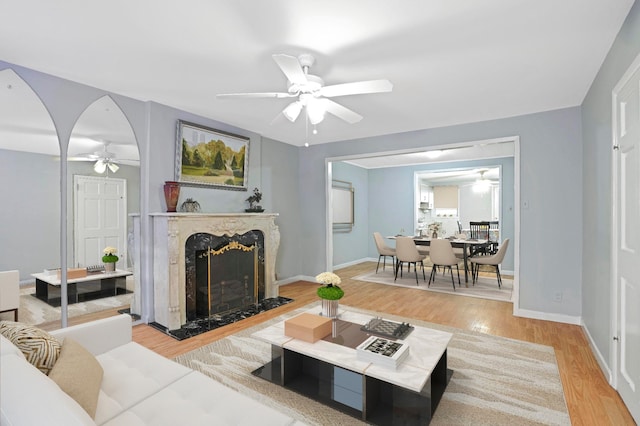 living room featuring light wood-style floors, ceiling fan, baseboards, and a premium fireplace