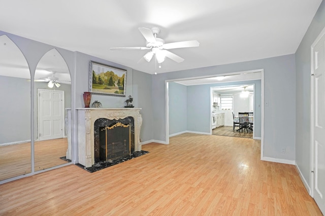 living area with light wood finished floors, baseboards, arched walkways, a ceiling fan, and a premium fireplace