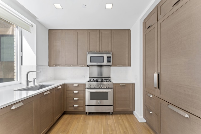 kitchen featuring light wood-style flooring, a sink, light countertops, appliances with stainless steel finishes, and tasteful backsplash