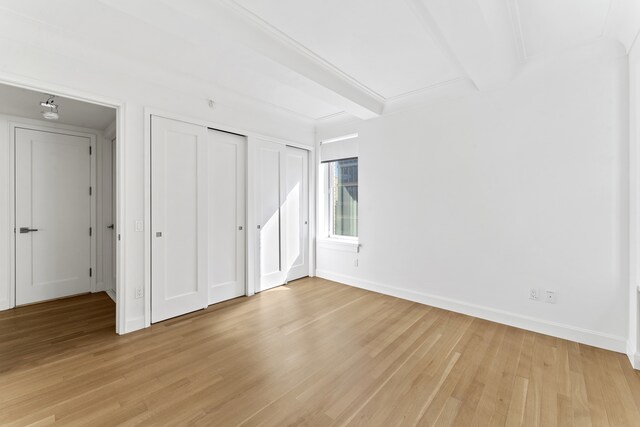 unfurnished bedroom with light wood-type flooring, two closets, beam ceiling, and baseboards