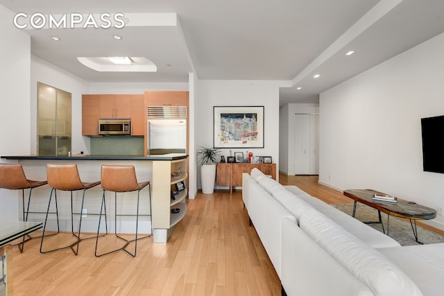 kitchen featuring a breakfast bar, light wood finished floors, tasteful backsplash, dark countertops, and appliances with stainless steel finishes