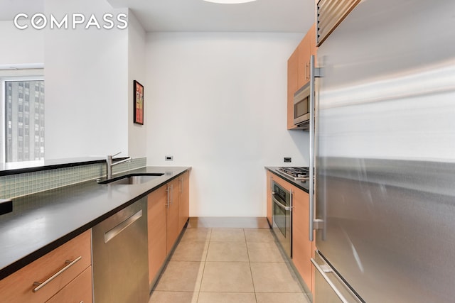 kitchen with light tile patterned floors, dark countertops, brown cabinets, stainless steel appliances, and a sink