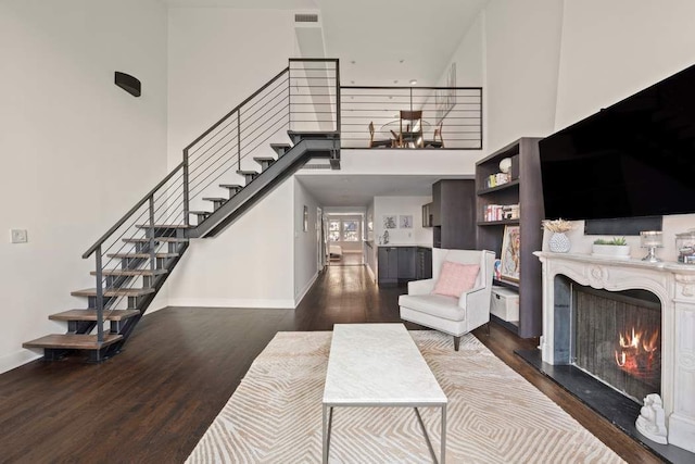 living area with wood finished floors, a high end fireplace, baseboards, a towering ceiling, and stairs