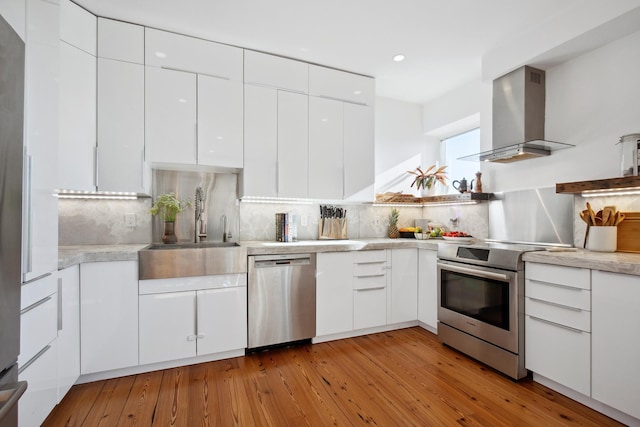 kitchen with a sink, stainless steel appliances, wall chimney exhaust hood, and white cabinets