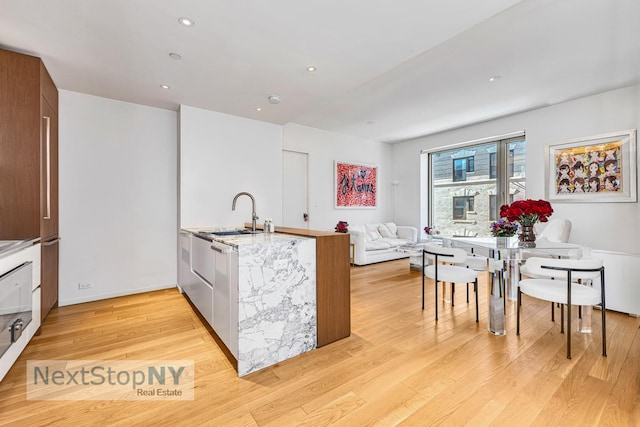 kitchen with light wood finished floors, modern cabinets, light countertops, a sink, and recessed lighting