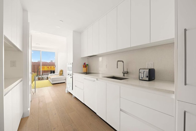 kitchen with light wood finished floors, white cabinetry, light countertops, modern cabinets, and a sink