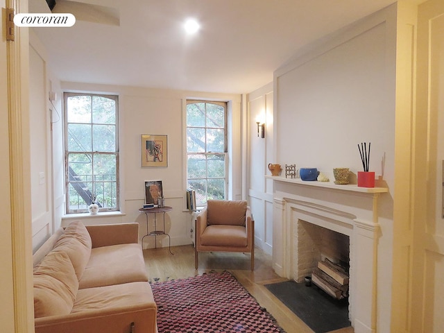 living area with a fireplace with flush hearth, a decorative wall, wood finished floors, and a healthy amount of sunlight