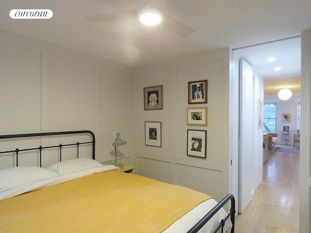 bedroom with light wood-type flooring, ceiling fan, visible vents, and a decorative wall