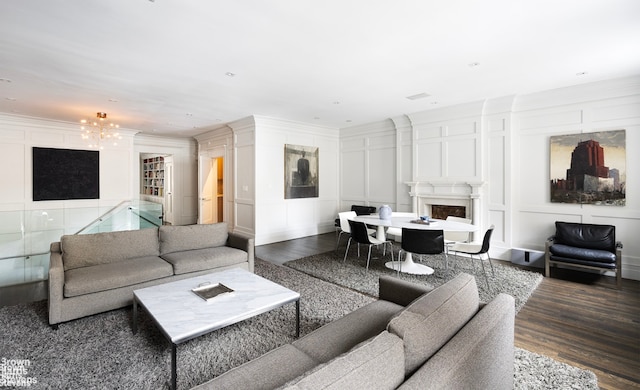 living area with a chandelier, a decorative wall, dark wood-style flooring, a fireplace, and ornamental molding