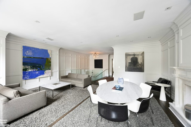 living area with a chandelier, dark wood-style floors, ornamental molding, and a decorative wall