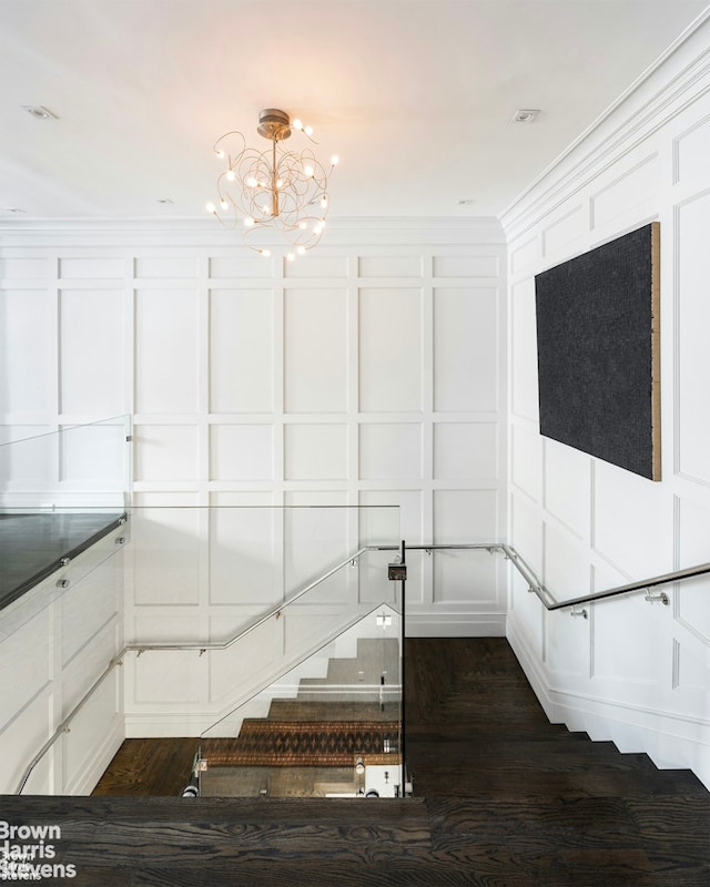 stairway featuring a notable chandelier, ornamental molding, and a decorative wall