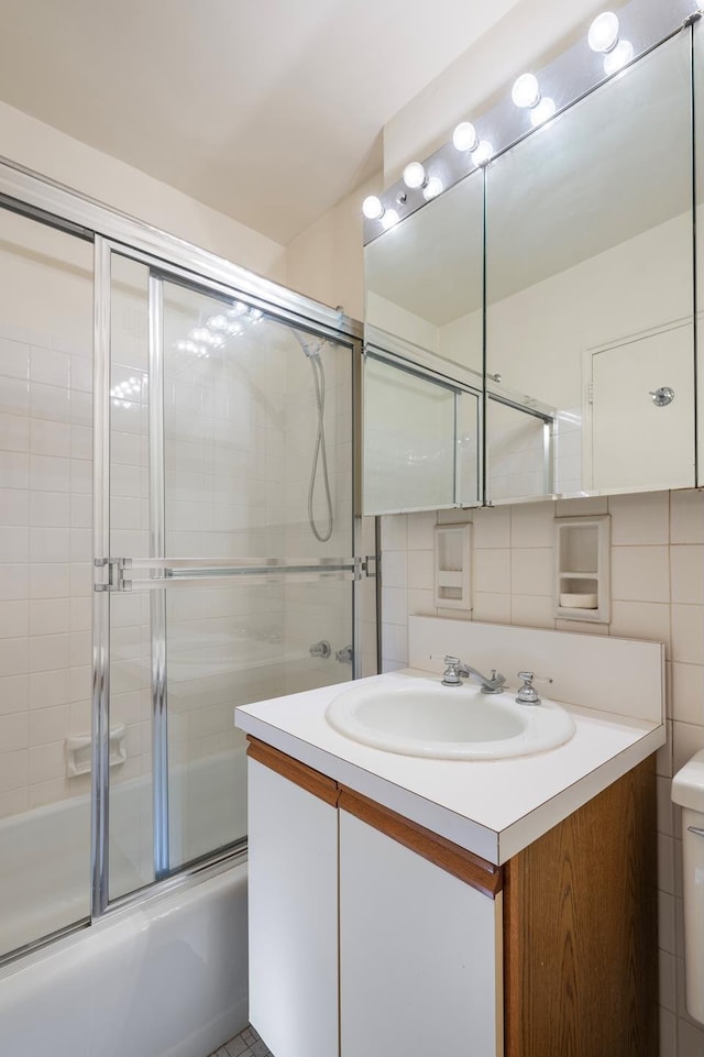 full bath featuring tile walls, bath / shower combo with glass door, decorative backsplash, toilet, and vanity