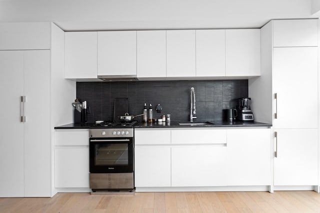 kitchen featuring stainless steel range with gas cooktop, modern cabinets, a sink, and white cabinetry