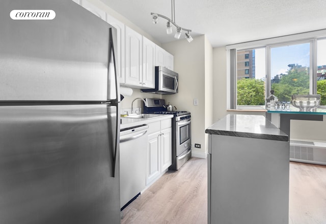kitchen with white cabinets, a sink, light wood-style floors, a textured ceiling, and appliances with stainless steel finishes